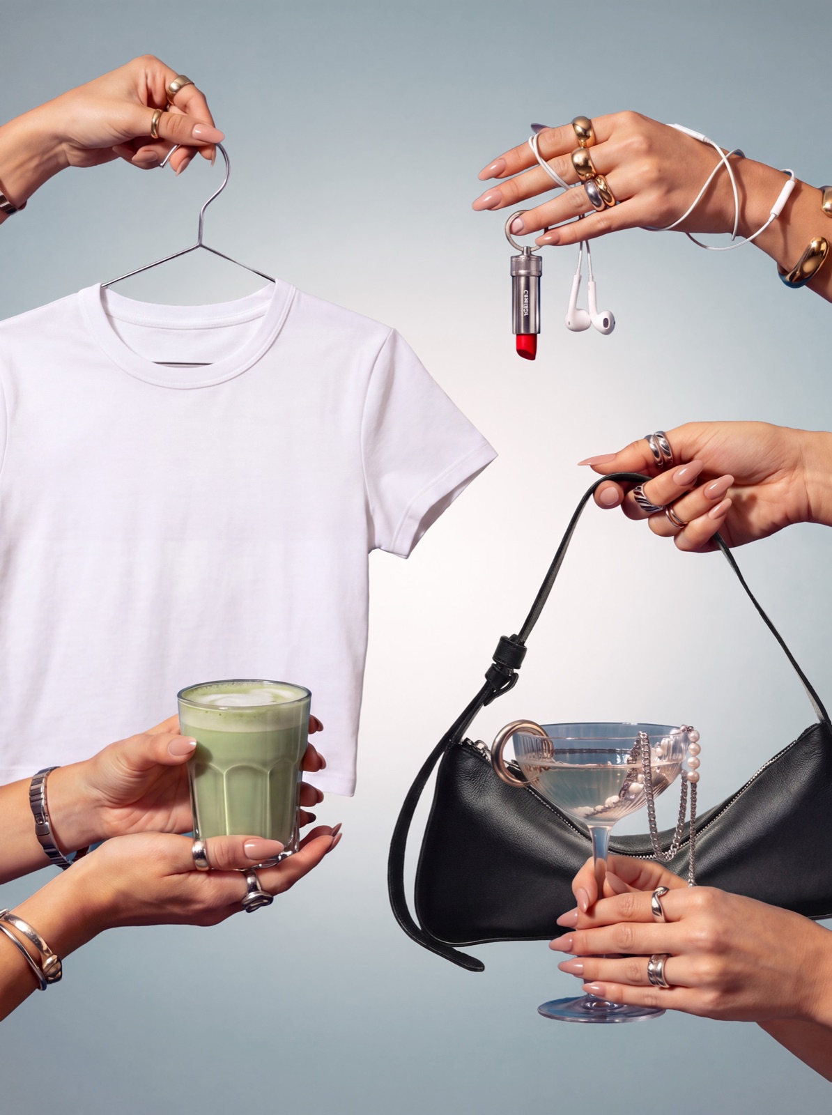 Hands holding up a white t-shirt on a hanger, a matcha latte, a black shoulder bag, a martini, a lipstick and earphones against pale grey-blue.