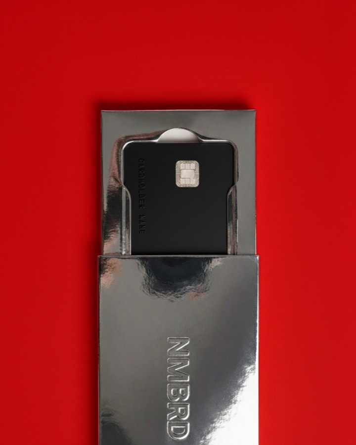 A black NMBRD key card sliding out of a silver sleeve on a red background.